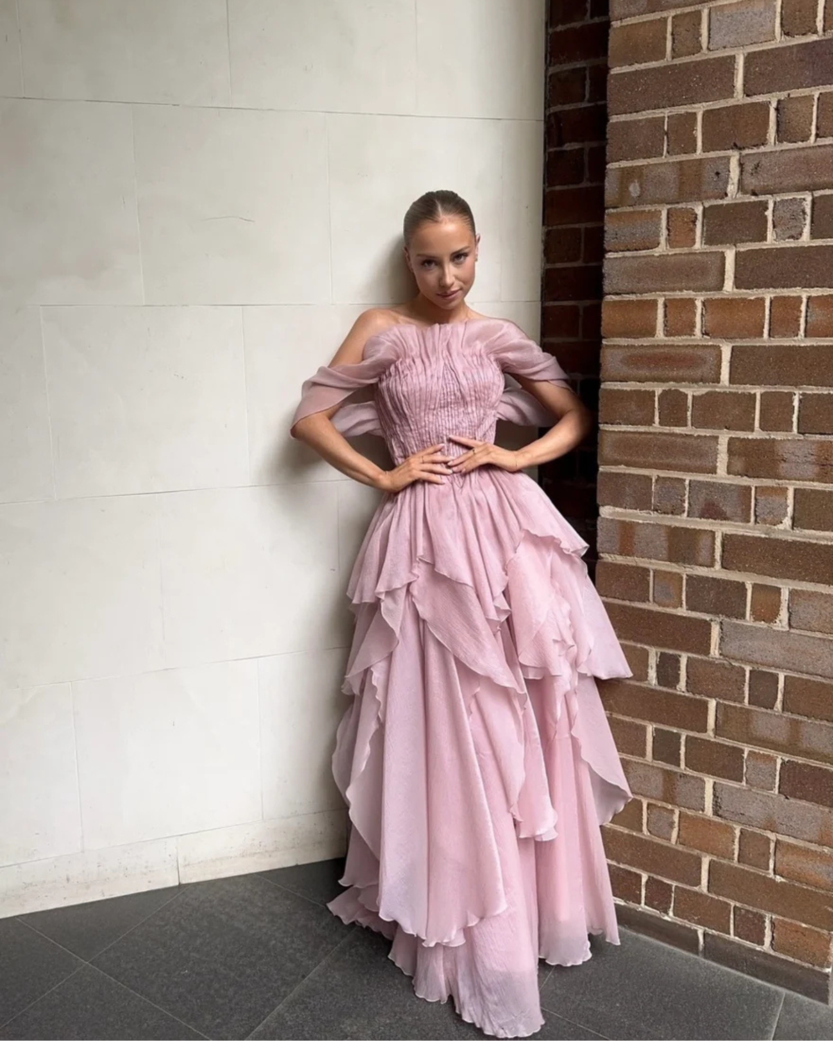 Aje Nisha Gown in fawn pink, lifestyle view against a brick wall