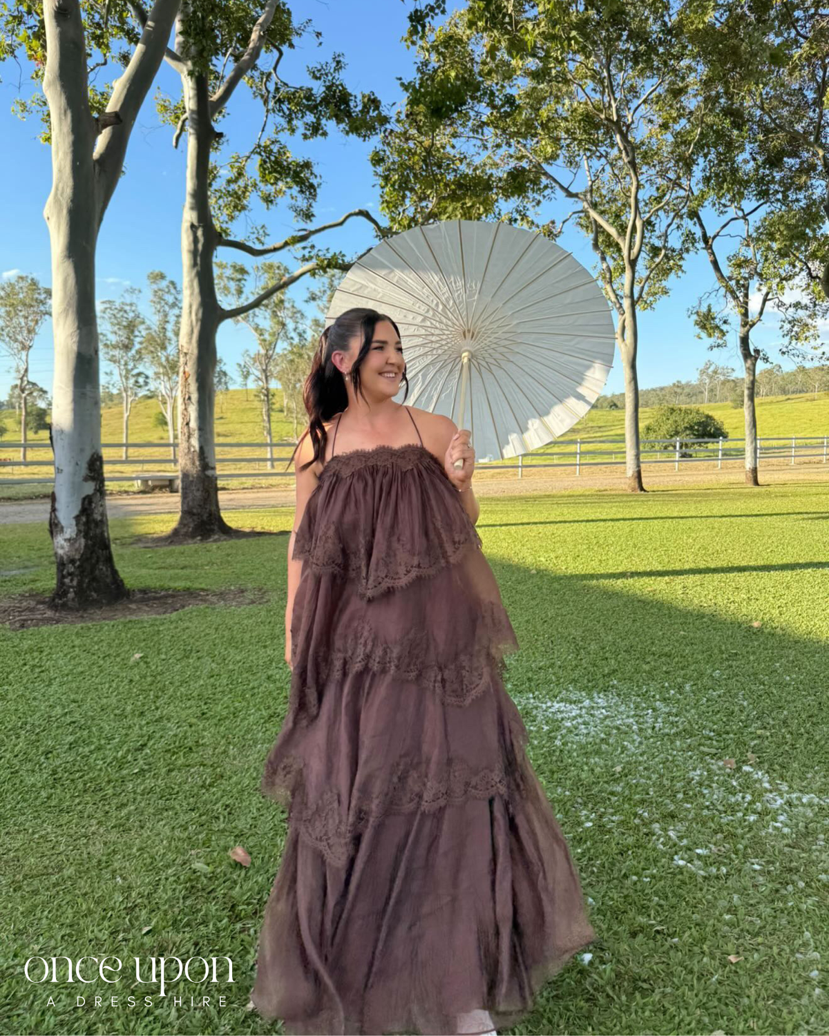 Aje Ophelia Lace Gown in chocolate brown, lifestyle view outdoors with a parasol
